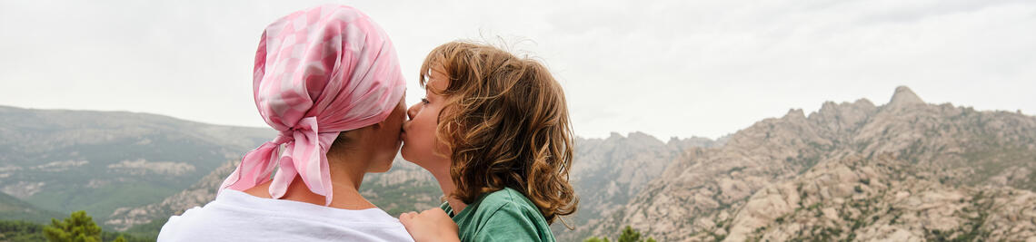 Woman with cancer relaxing in nature. She is with her son who is giving her a kiss.
